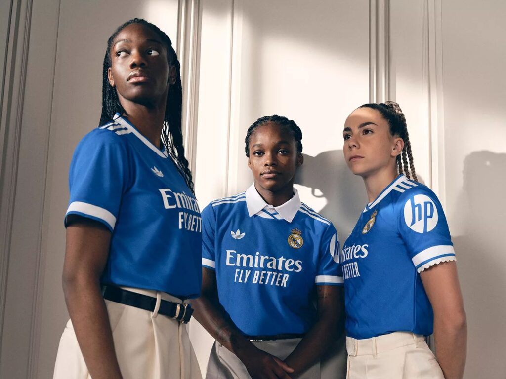 Three Real Madrid woman's players styling the new light blue Real Madrid jersey with a white wall in the background.