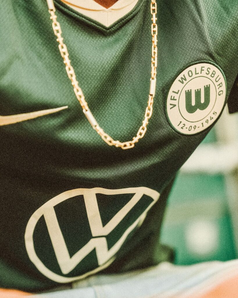 Forrest green Wolfsburg jersey close up with vintage badge and person wearing a gold chain.