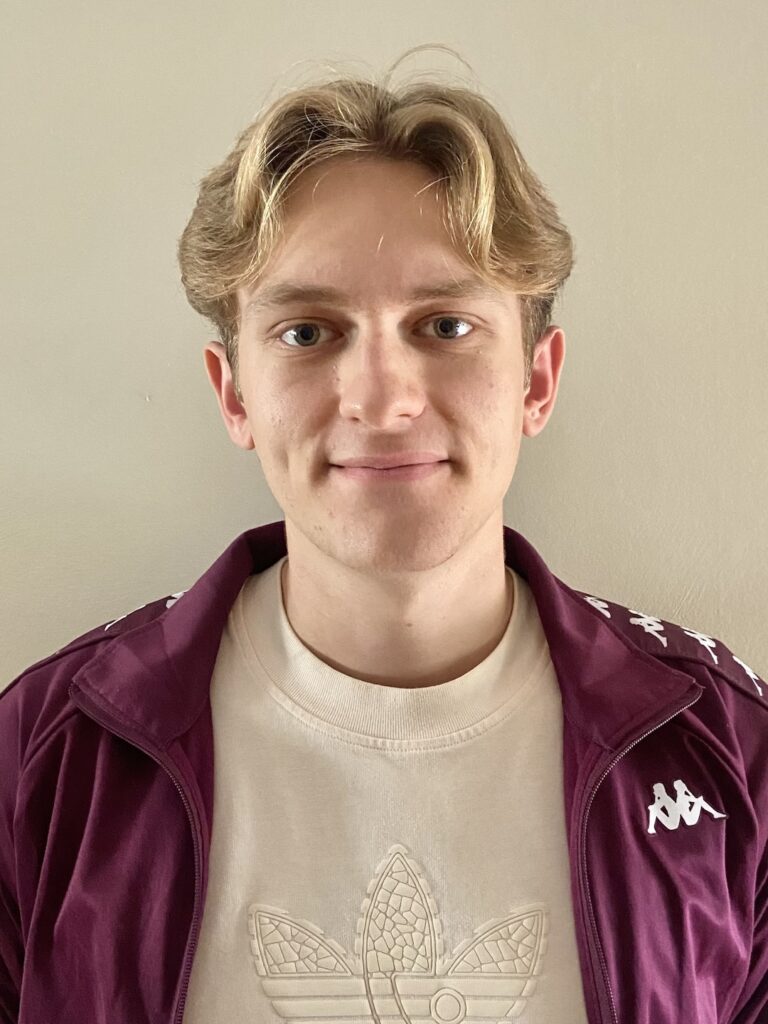 Headshot image of Kits and Culture Founder. Blonde haired male wearing a purple sweatshirt and a cream shirt.